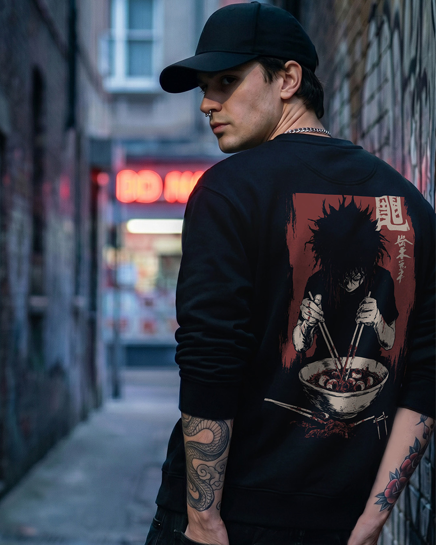 Black sweatshirt with anime-style back print of a dark-haired character eating ramen, featuring red Japanese kanji accents, modeled in a moody urban alleyway with neon signage.